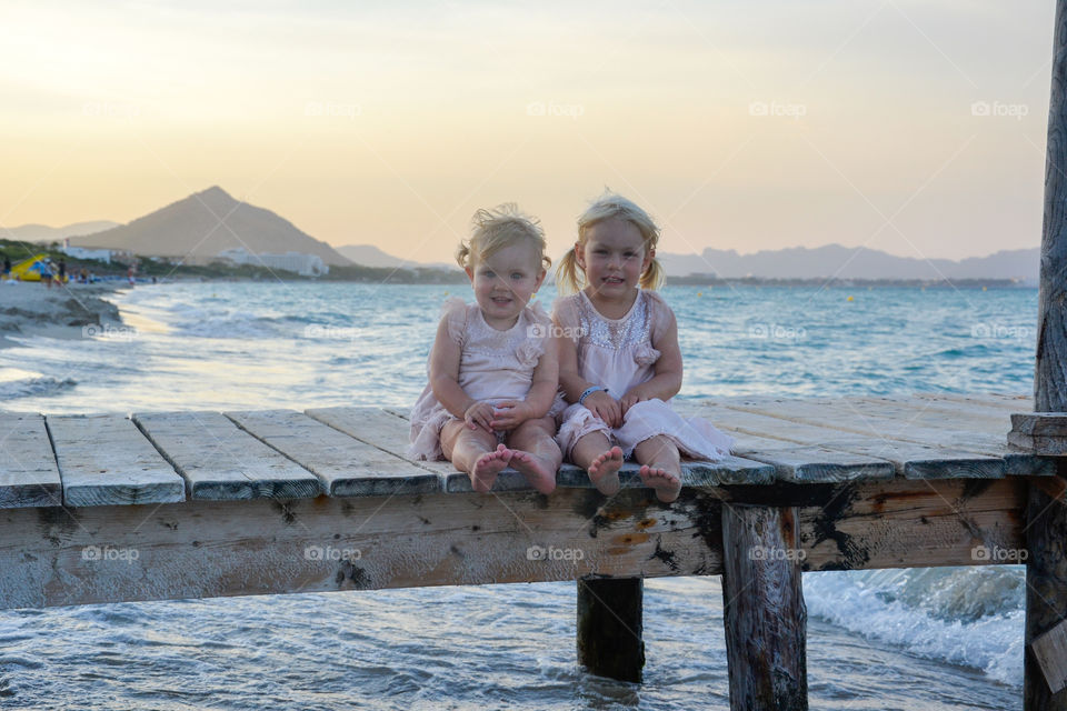 Two little sister sitting on a bridge smiling and looking cute in Alcudia, majorca.