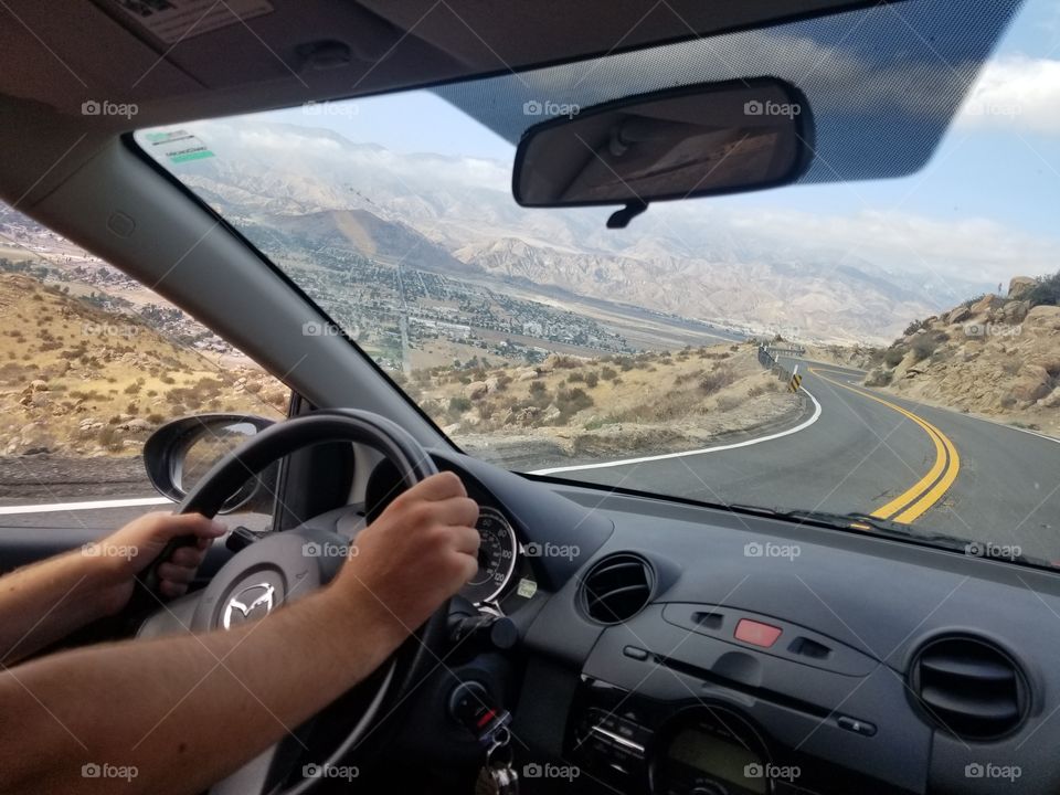 Hands on the wheel of a Mazda 2 during a roadtrip over a curvy mountain road.
Mazda logo.