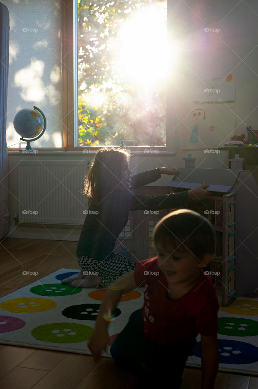 Children playing with doll house in their room during evening sunshine lurking through the window.