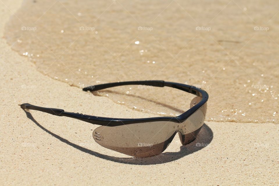 sunglasses under wet sand near waves