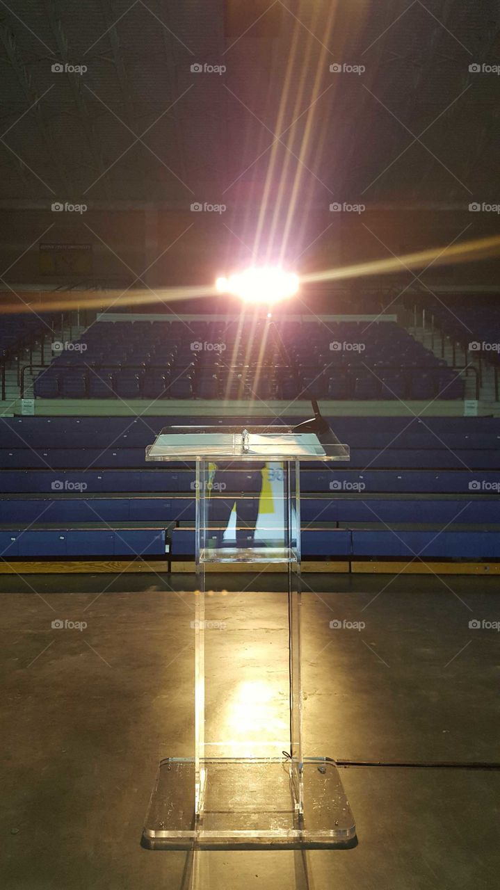 a clear Podium sits in front of empty bleachers with spot light shining on it