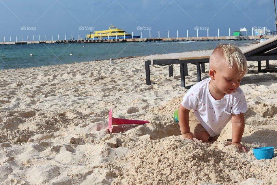 Blond boy playing with sand at the Caribbean Sea 