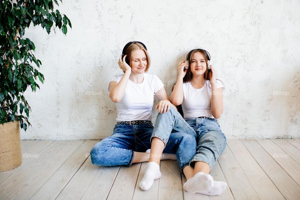 Two teenage girls in jeans listening music in earphones. Siblings