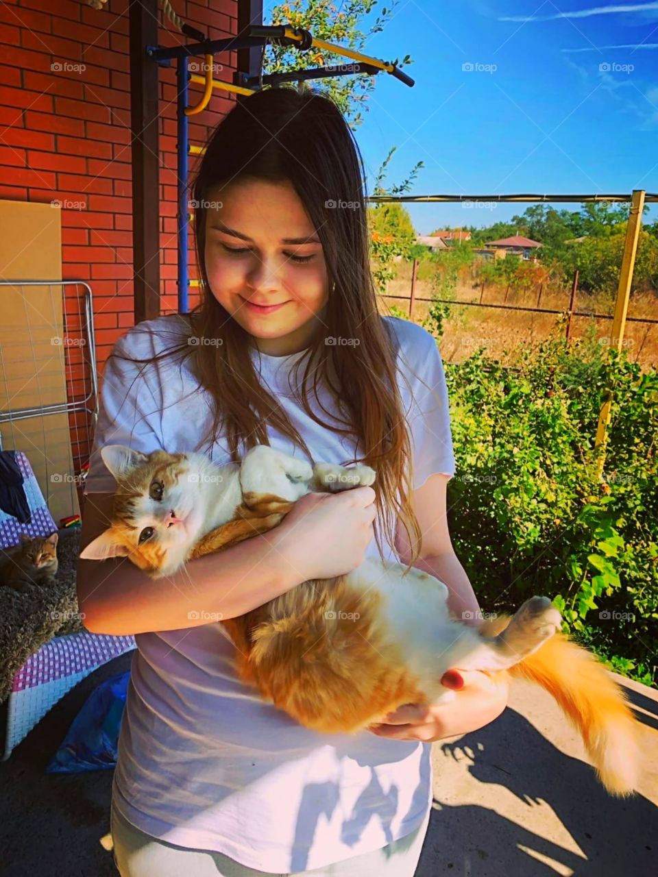 A young girl is holding a ginger cat and smiling.  sunny day