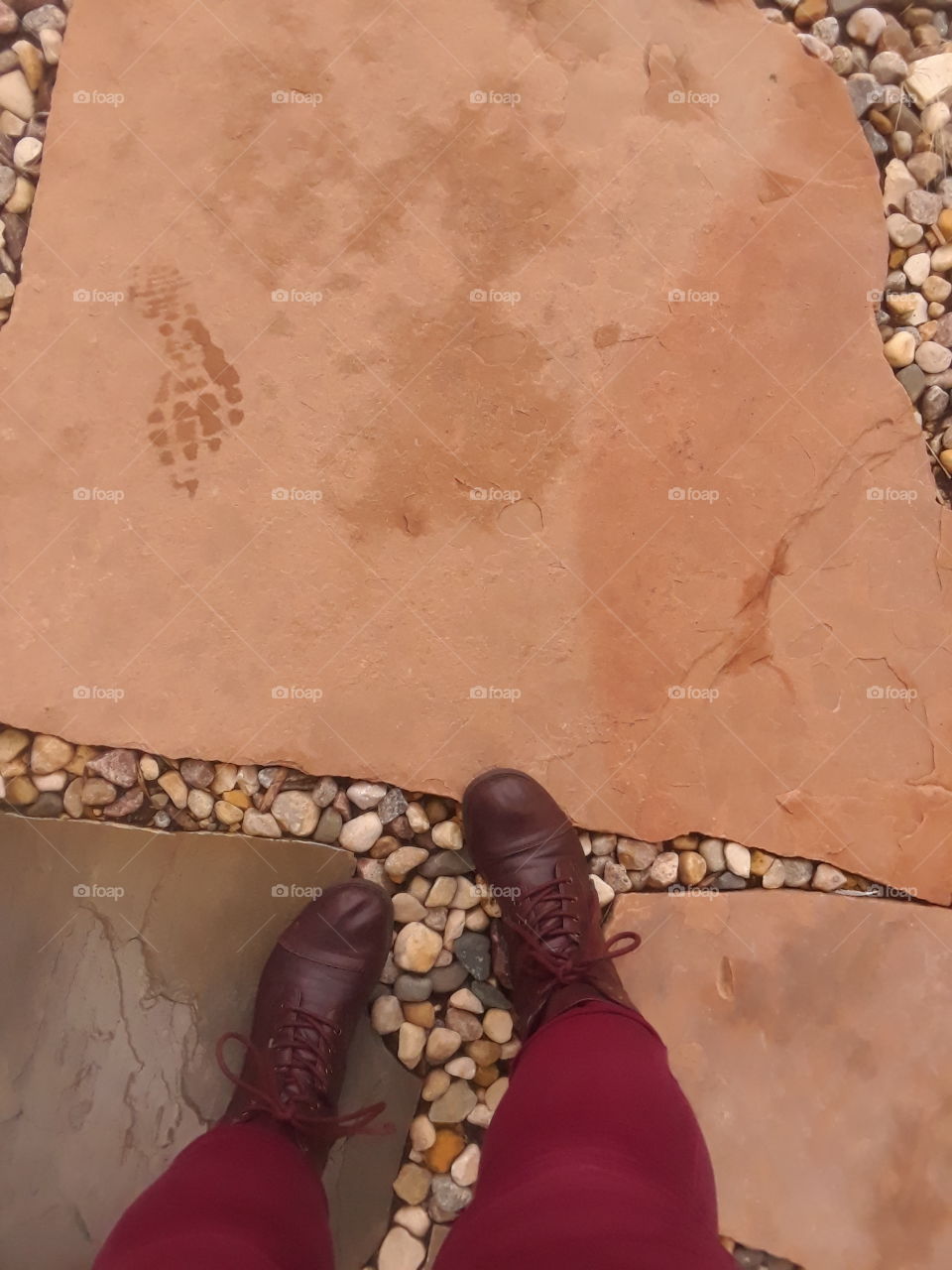 downward looking image of brown combat boots with red pants walking along an orange large stone pathway