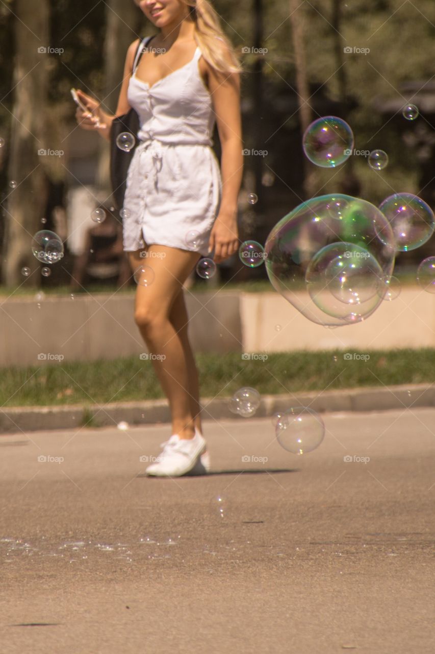 Woman walking with her phone in her hand in between the bubbles 