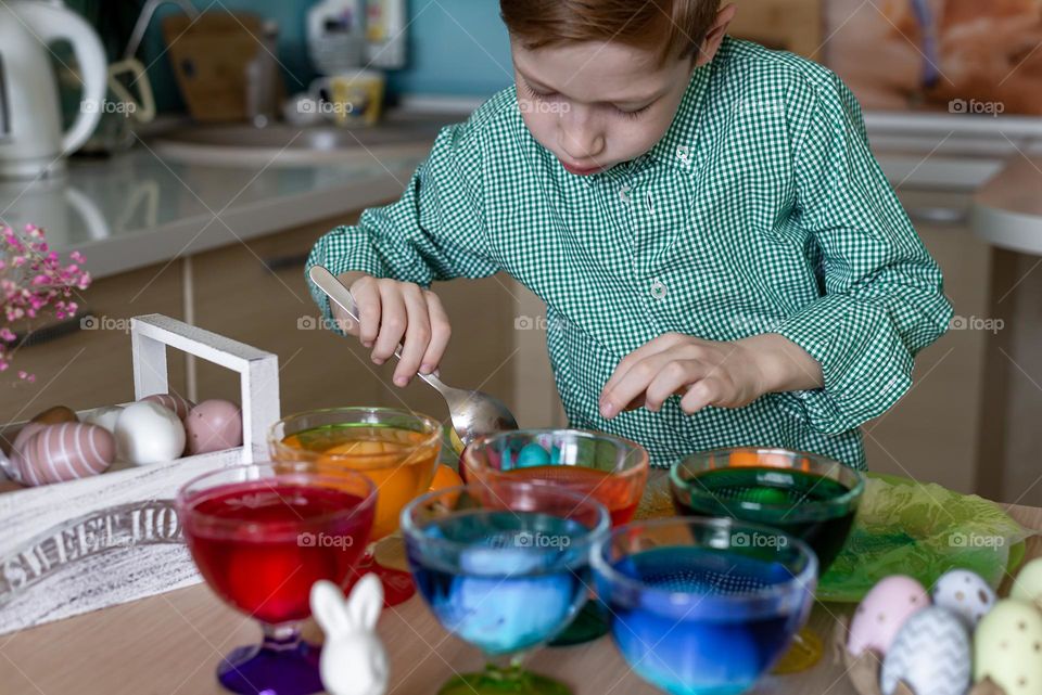 Easter traditions. Red-haired boy paints eggs in the kitchen