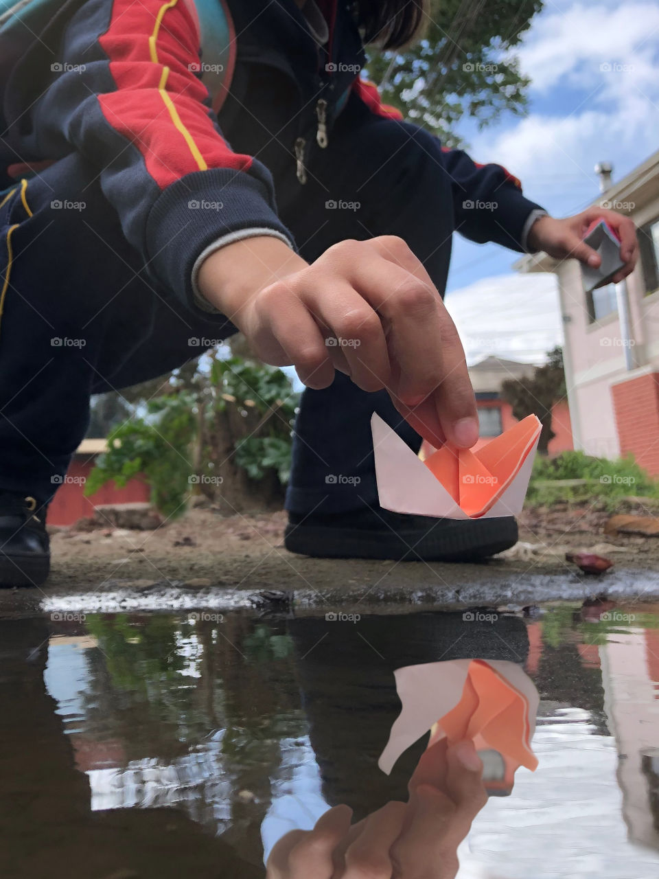 little girl putting her origami boat in a puddle of water