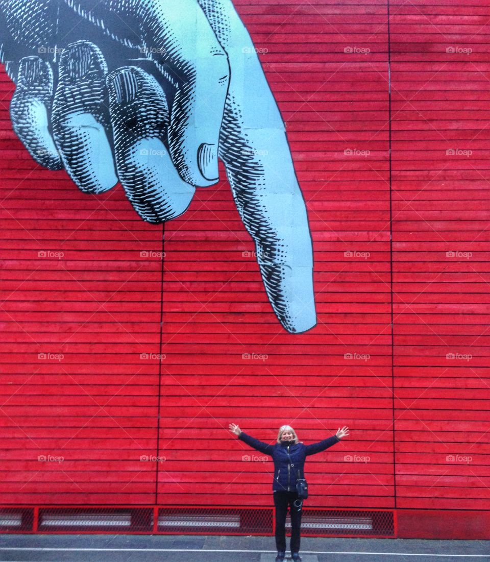 Woman standing against wall with a finger pointing at her