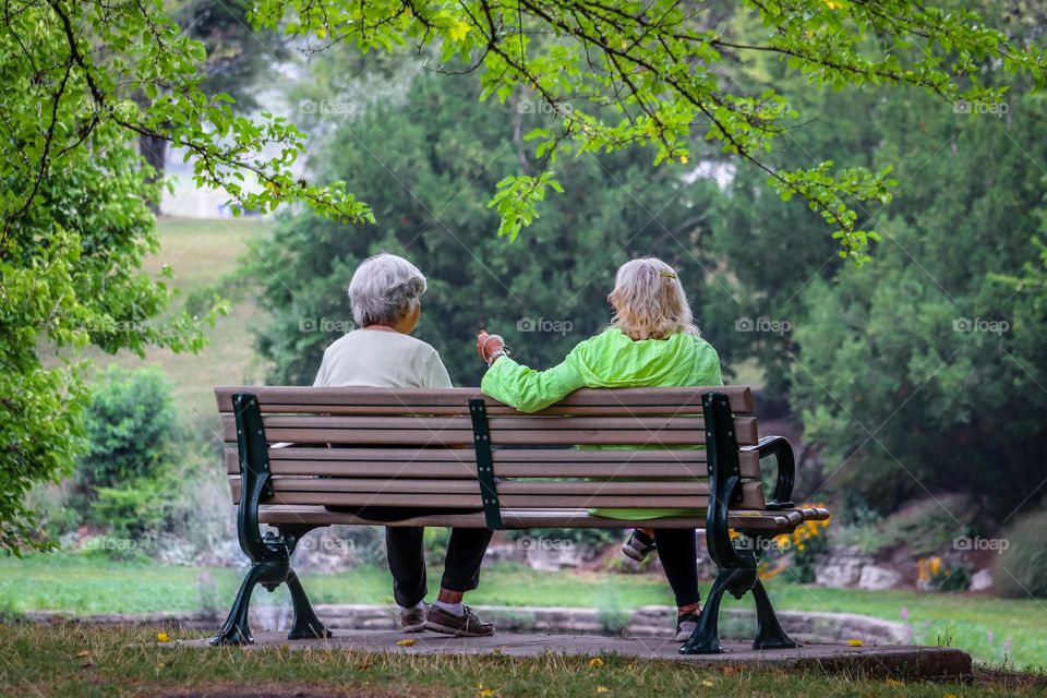 Two elderly ladies talking to each other sitting on a bench in the park