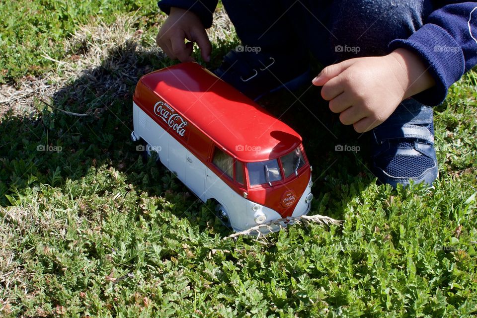 Coke VW bus and a child playing with it outdoors in the grass