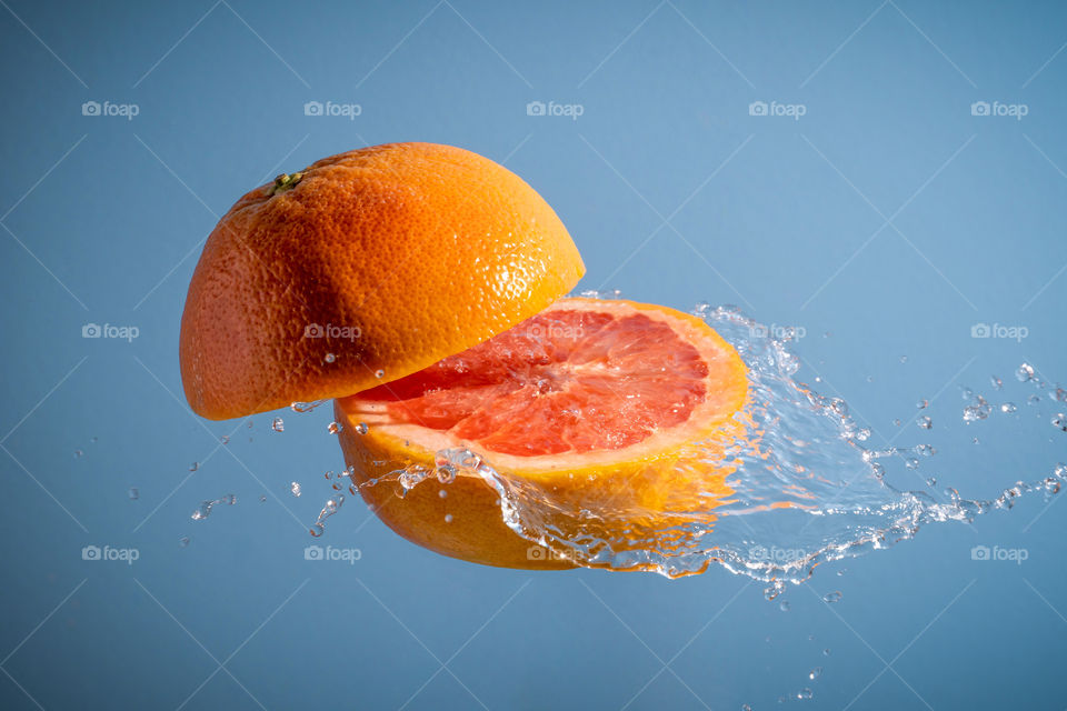 Grapefruit sliced in air with juice splashing. Blue background. Creative summer or fruit concept