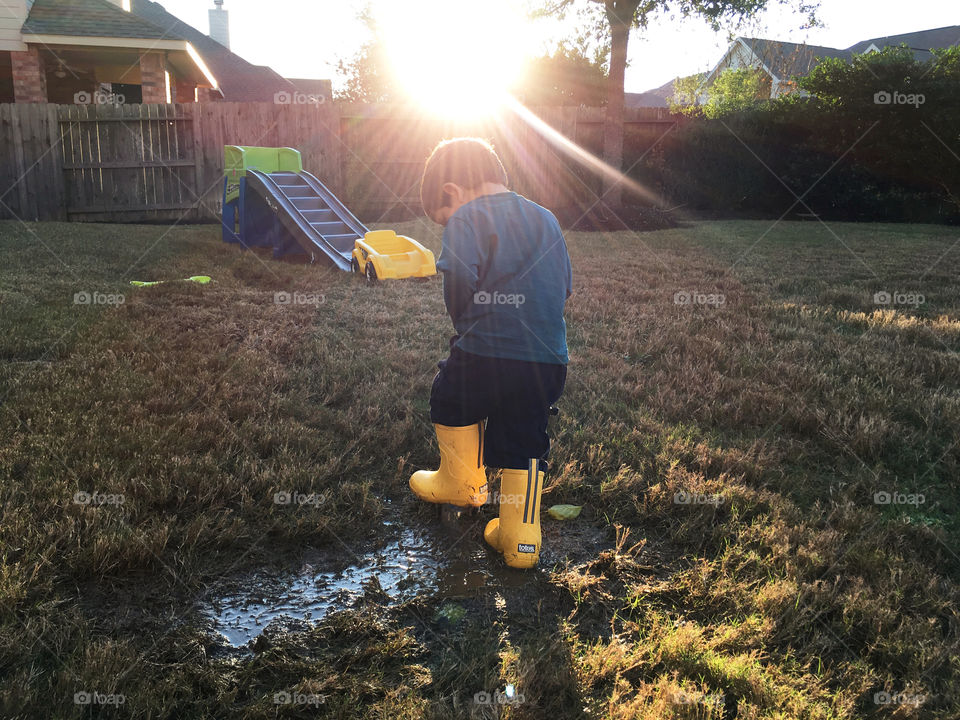 Boy playing in puddle at sunset wearing yellow rain boots