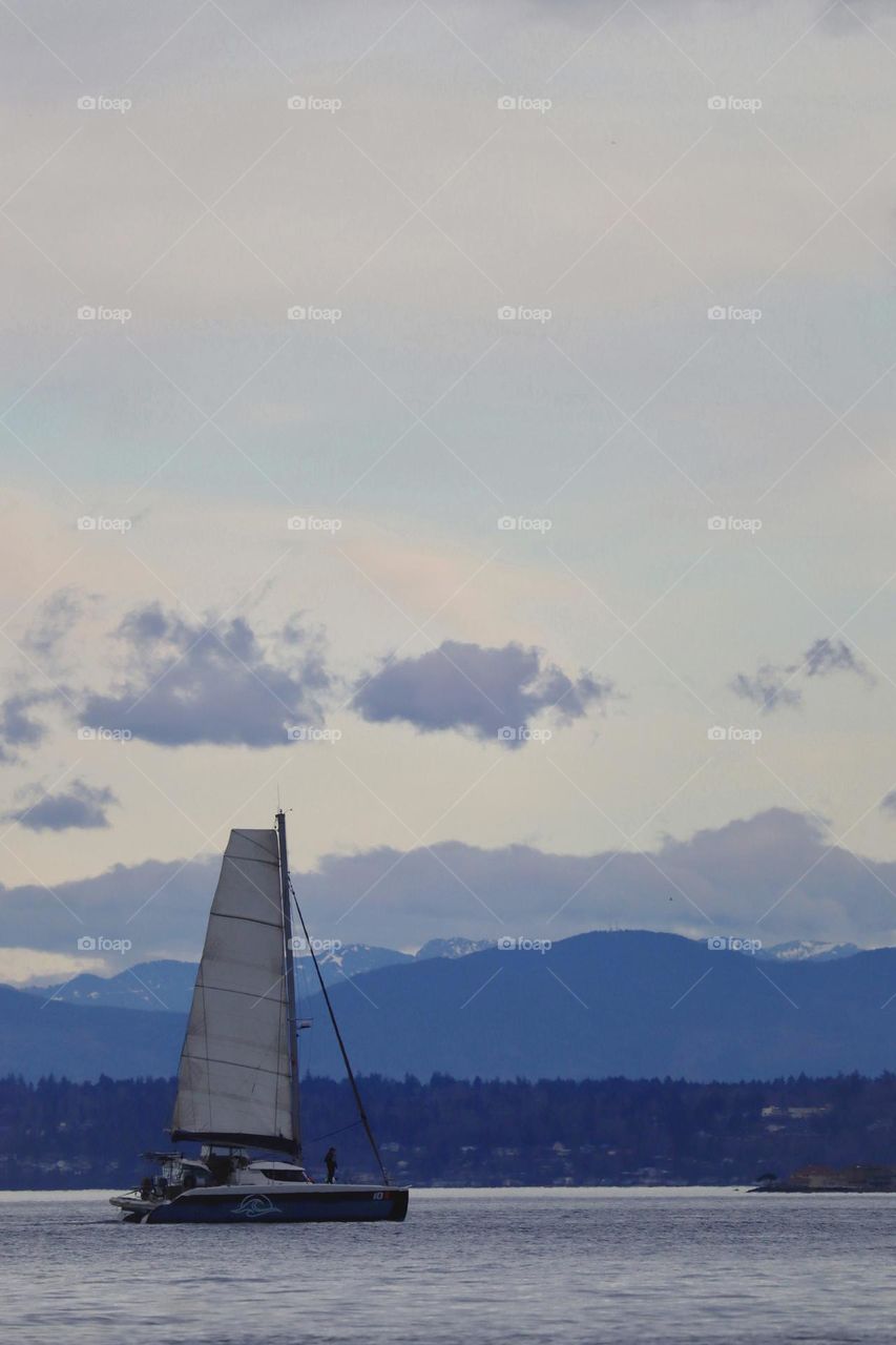 Commencement Bay is all shades of blue as a sailboat cruises through and evening arrives. Tacoma, Washington 