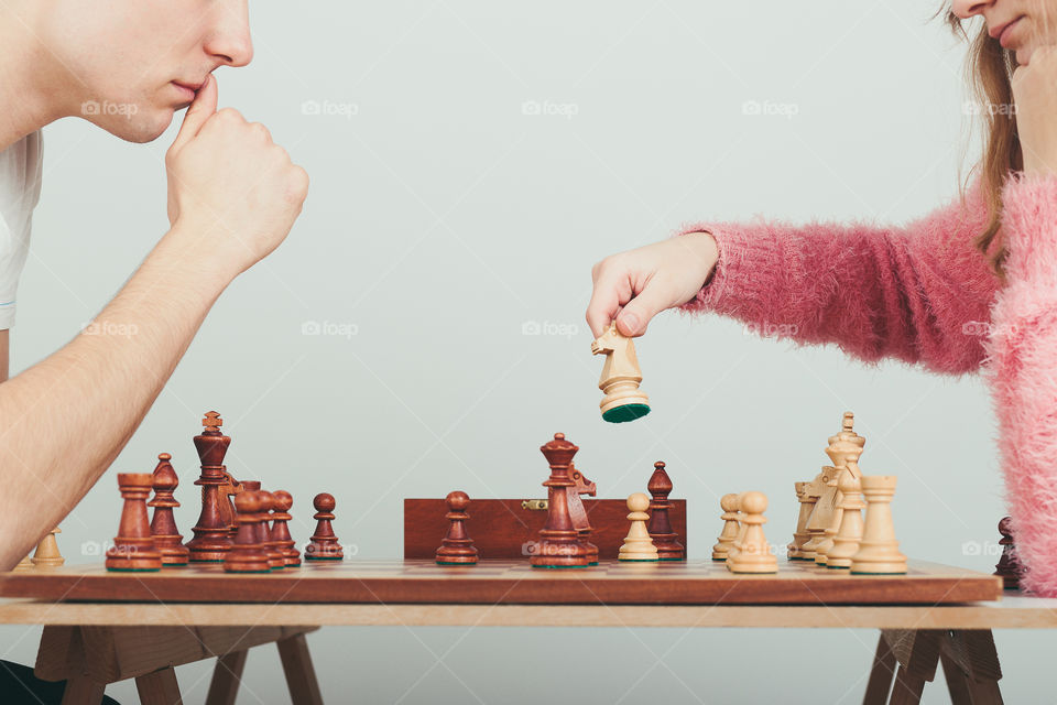 Girl and boy playing chess at home. Girl moving her piece. Teenagers sitting by a table. Profile view. Copy space for text at the top and bottom of image
