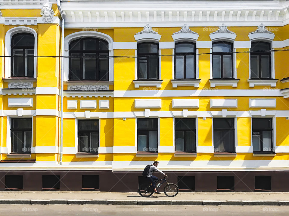 Young man riding a bicycle and using mobile phone in front of yellow old building 