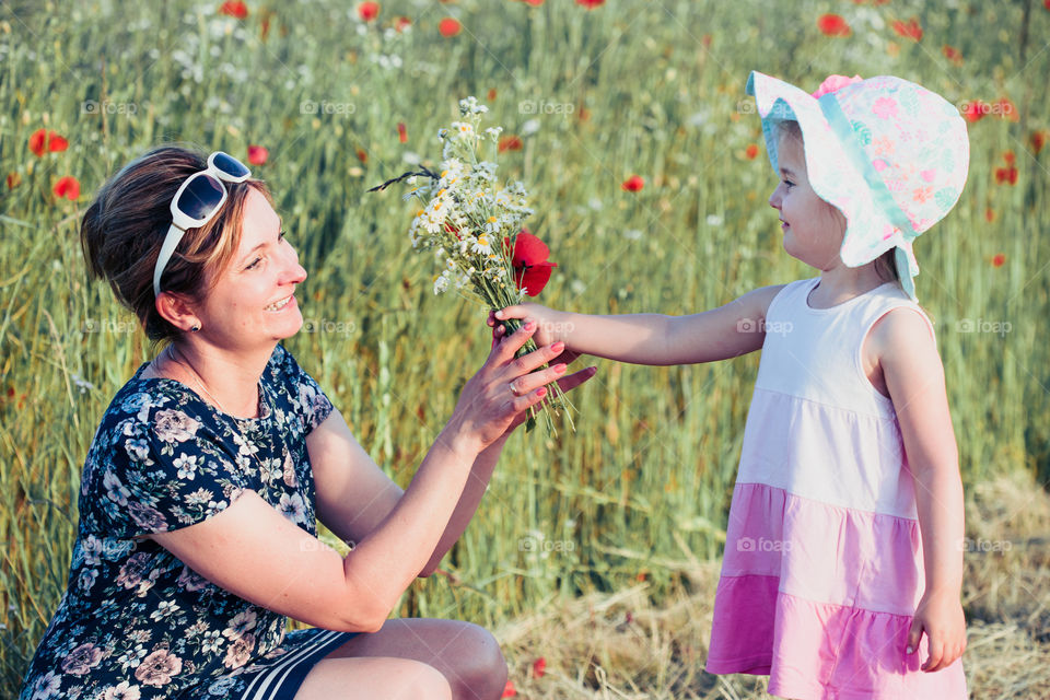 Mother and her little daughter in the field of wild flowers. Little girl picking the spring flowers for her mom for Mother's Day in the meadow. Girl handing the flowers to her mom. Nature scene, family time