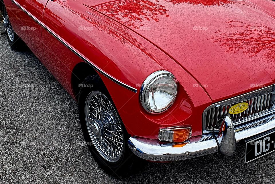 Part of the front of a red MG MGB showing a front light and tyre, the grill at Cherbourg car show
