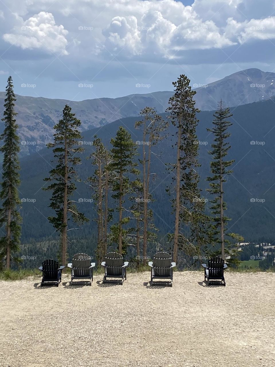 Five chairs on a mountain overlooking pine trees and other mountain peeks. 
