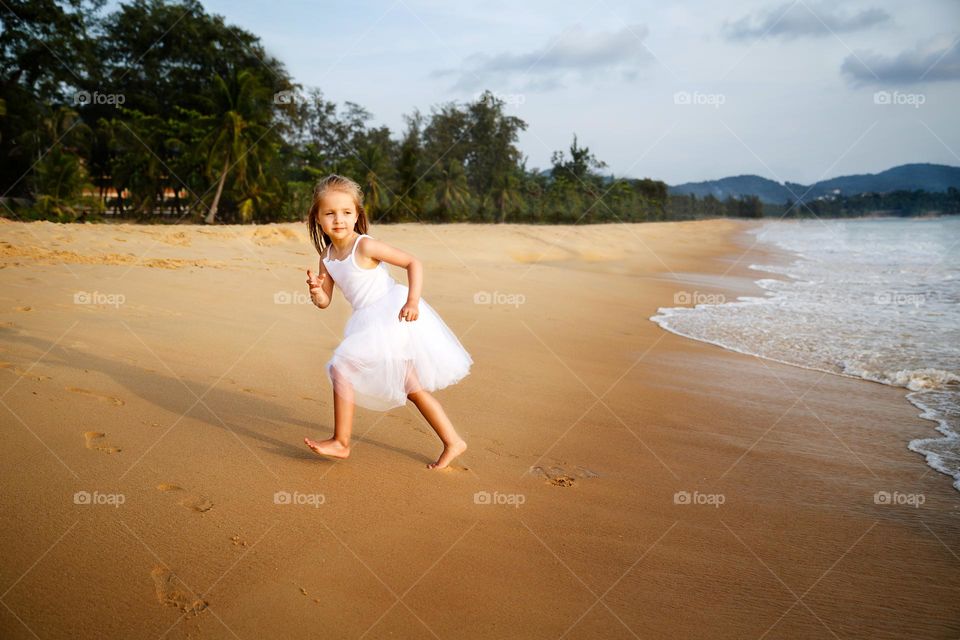 Happy little Caucasian girl with blonde hair having fun on sea at hot summer day 