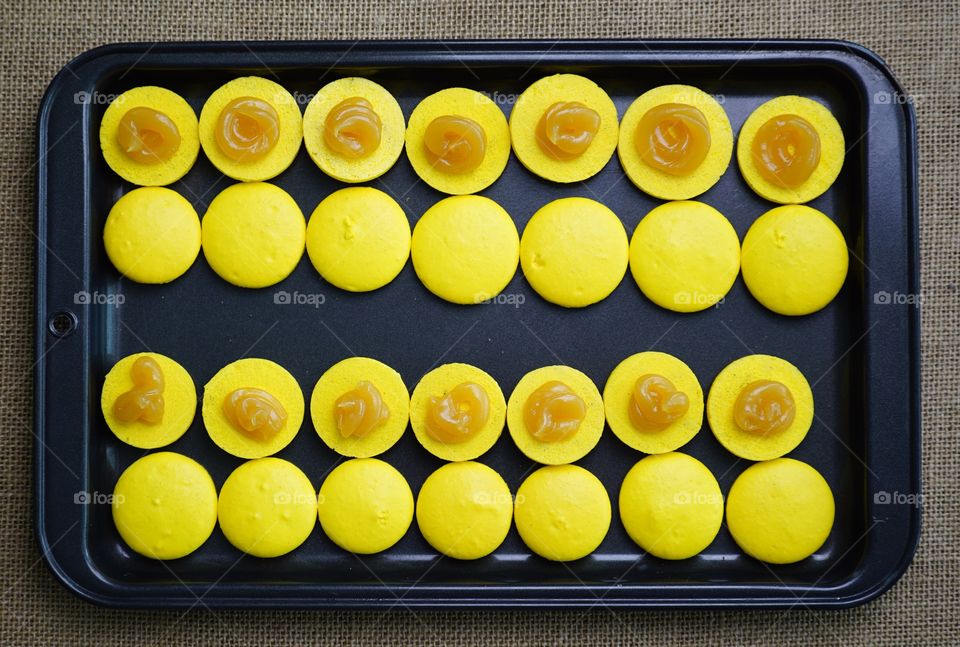 Bright yellow macarons on the black baking tray, fresh from the oven.