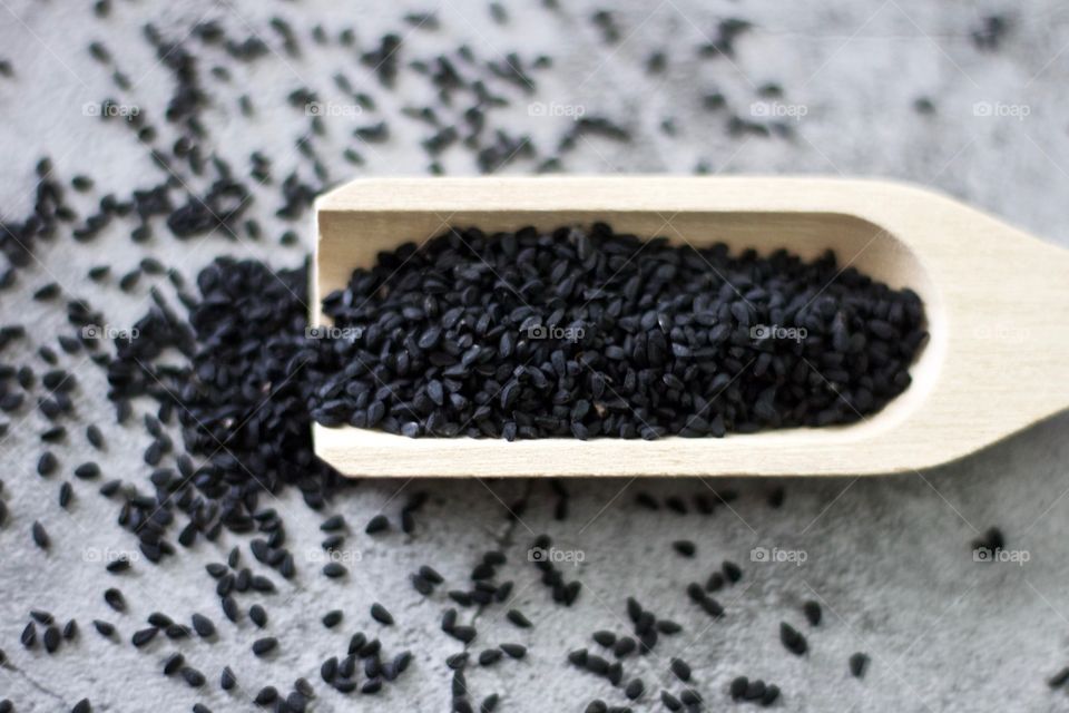 Overhead view of black seed spilling out of a wooden scoop on stone surface 