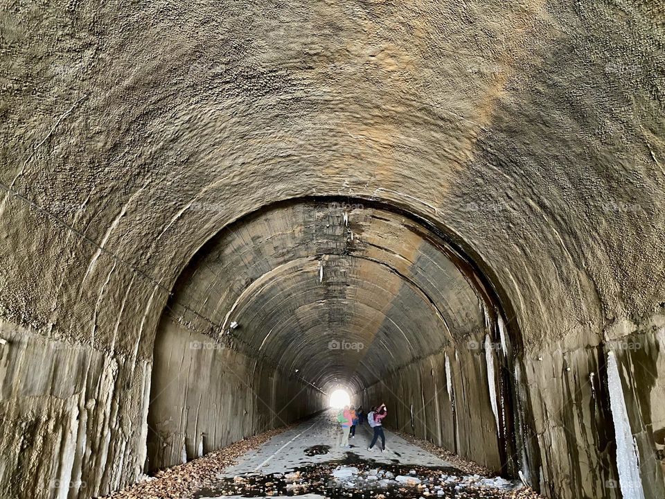 People taking pictures inside an old railway tunnel with icicles on the walls