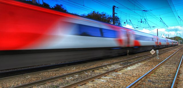 A passenger express train speeds past underneath electric wires and is blurred by motion blur.