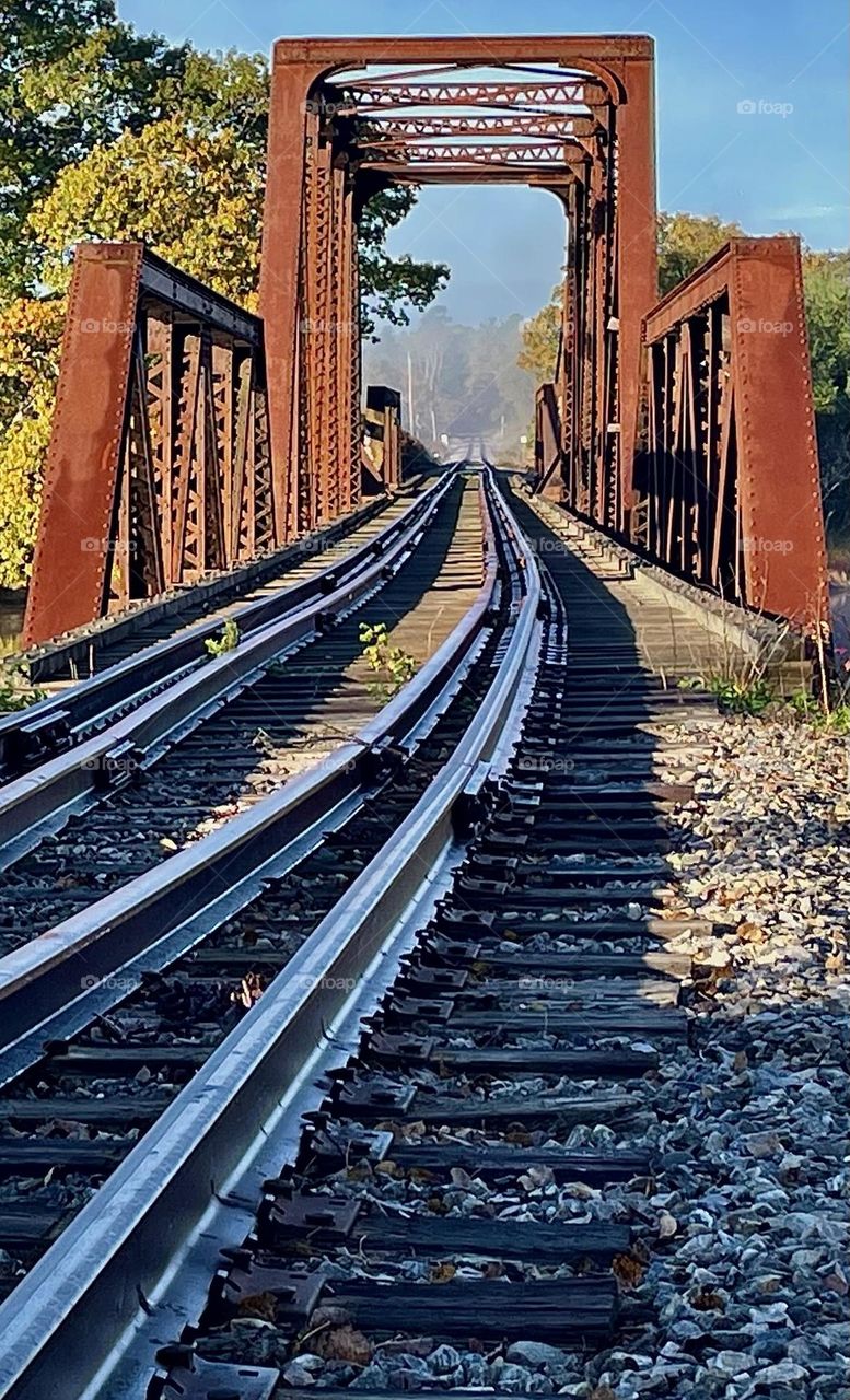 Train tracks curve into a trestle bridge before disappearing into the morning fog beyond.