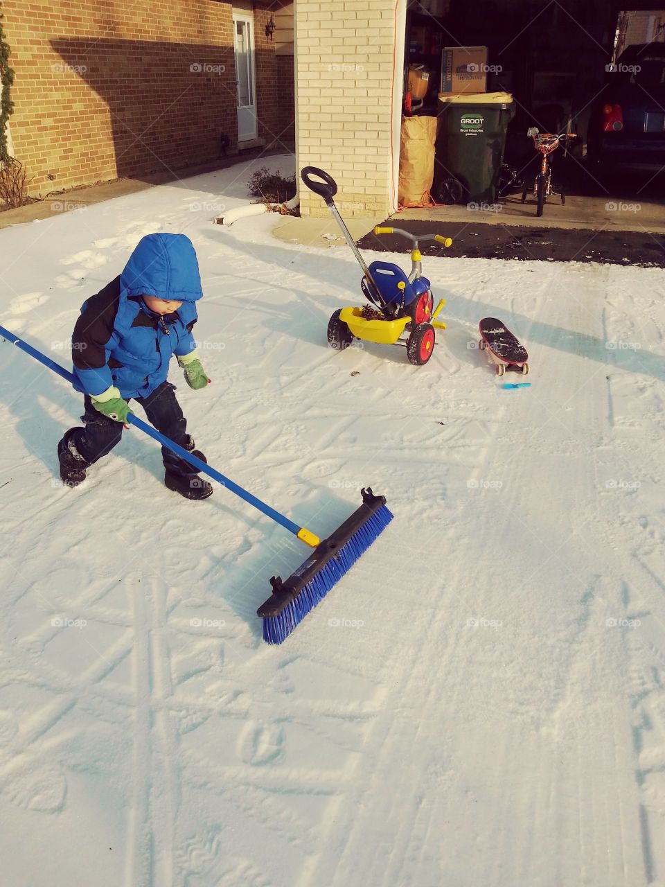 small boy sweeping snow in driveway with broom