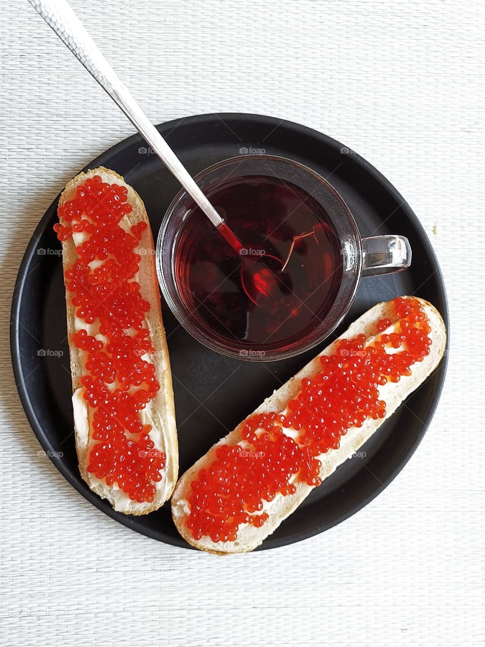 On a tray: a cup of tea and two sandwiches with red caviar