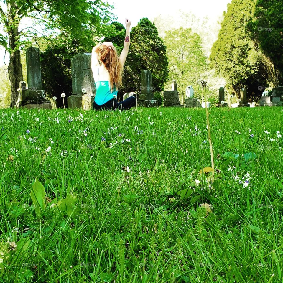 The back of a red haired girl doing yoga in a secluded cemetery