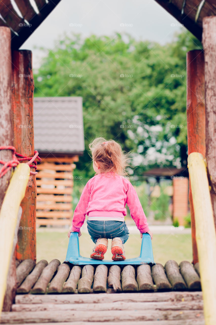 Little toddler girl playing in the playground standing on slide