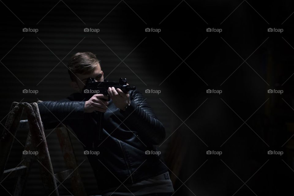 young man in dark garage pointing with gun on someone