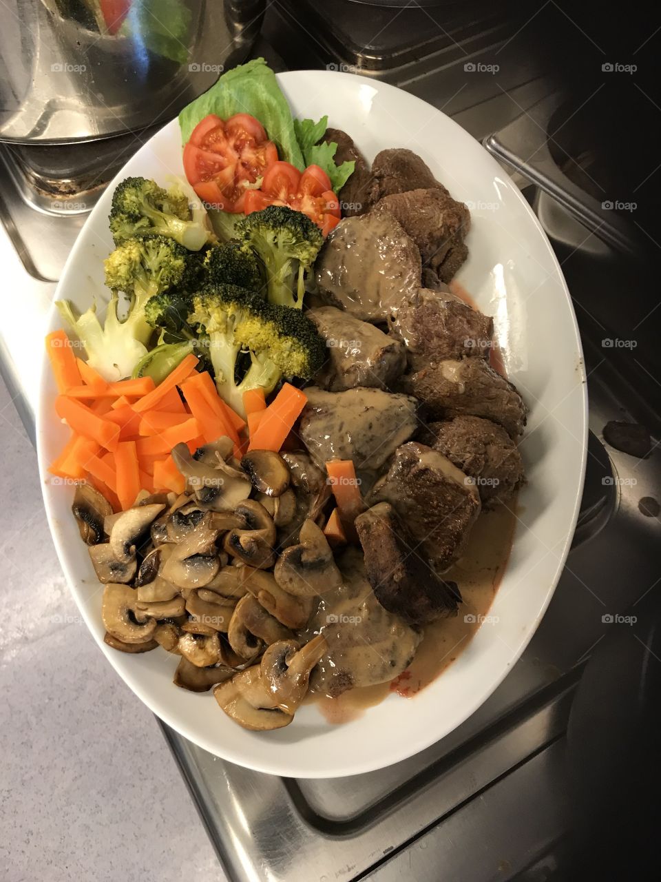 Dinner ready to be served at a restaurant. There is some carrots, broccoli, tomatoes, mushrooms and really tasty steaks.