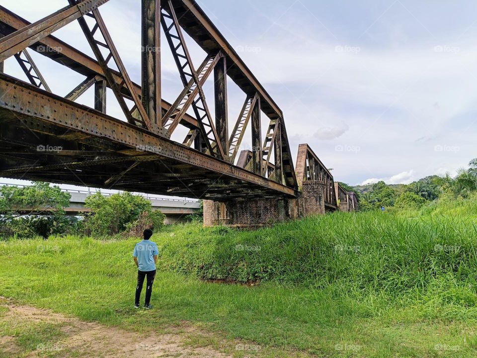 A young man standing under the old railway bridge.