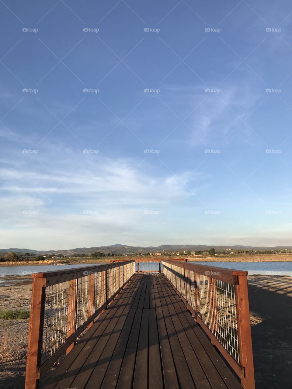 A wooden viewing bridge extends to a pond in a wildlife park outside of Prineville in Crook County in Central Oregon with the golden glow of evening on a fall day. 