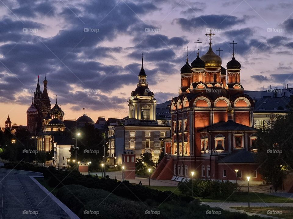Nightly view of buildings with lit windows; domes and cuppolas against a cloudy sky