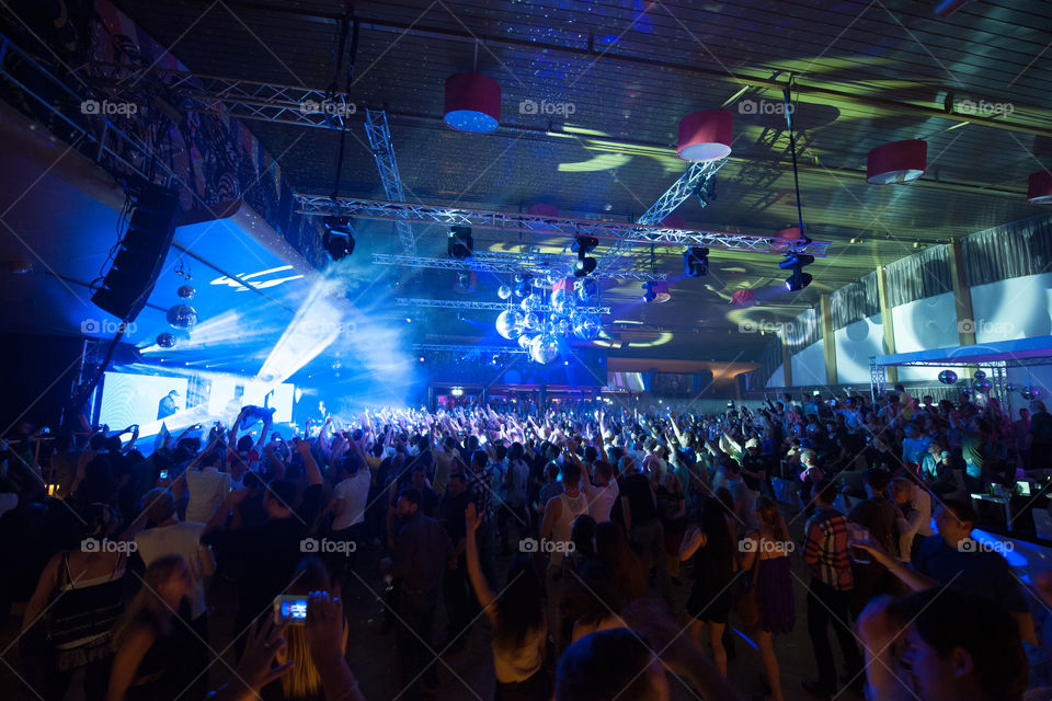 Big nightclub with thousands av people partying with live performance of a DJ