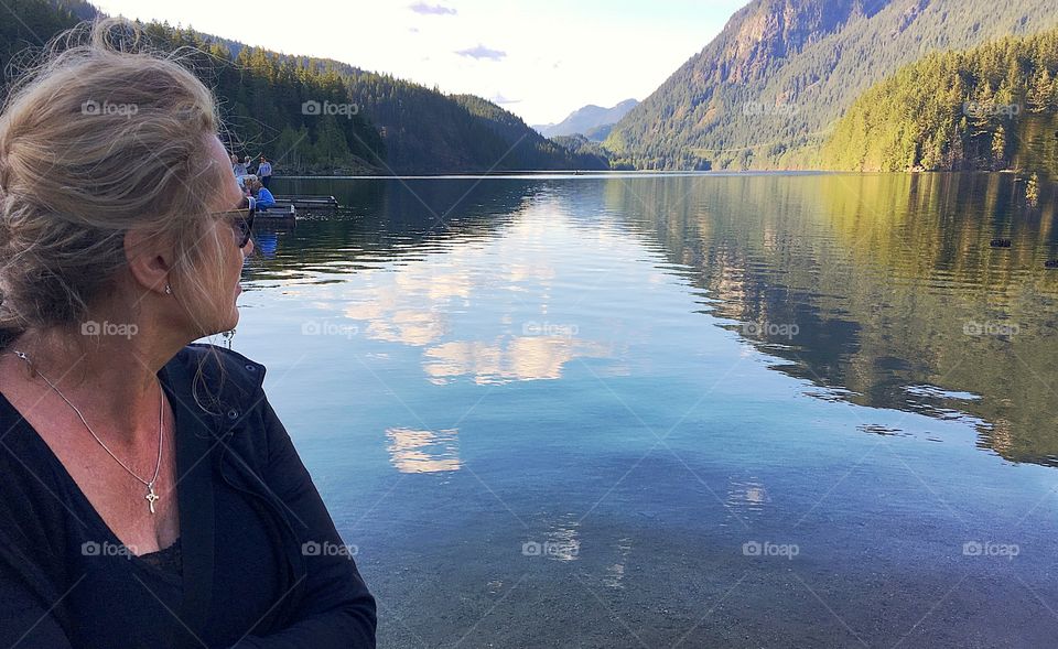 Blonde woman looking at beautiful reflections and mountains at lake