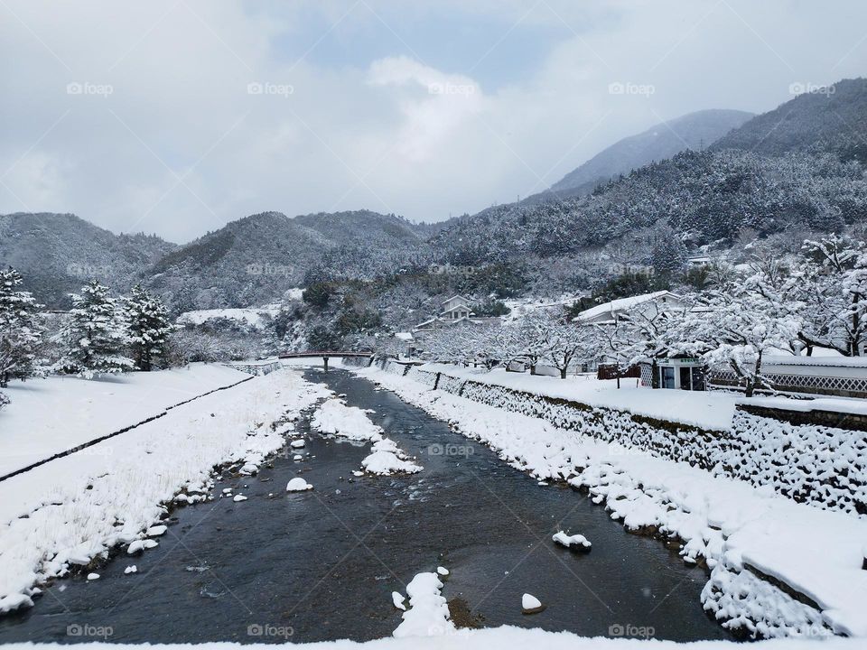 A river winds through a snowy landscape, surrounded by white hills and frost-covered trees. A peaceful and enchanting winter scene.