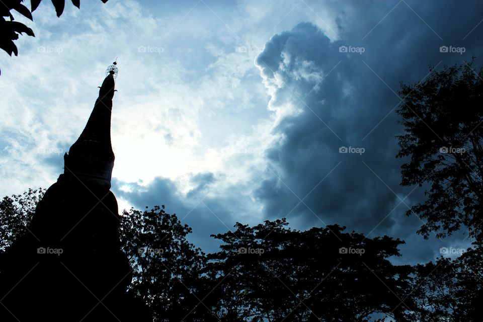 Black pagoda silhouette among the trees and the atmosphere in the sky with clouds forming rain. Silhouette and nature.
