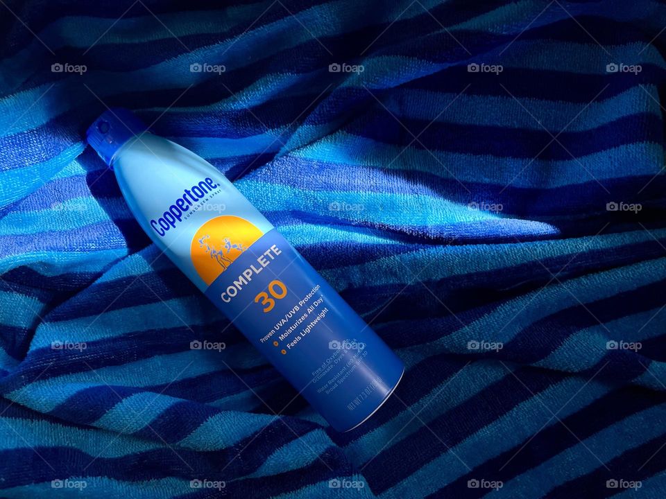 Sun protection spray Coppertone on the blue towel in Sun light 