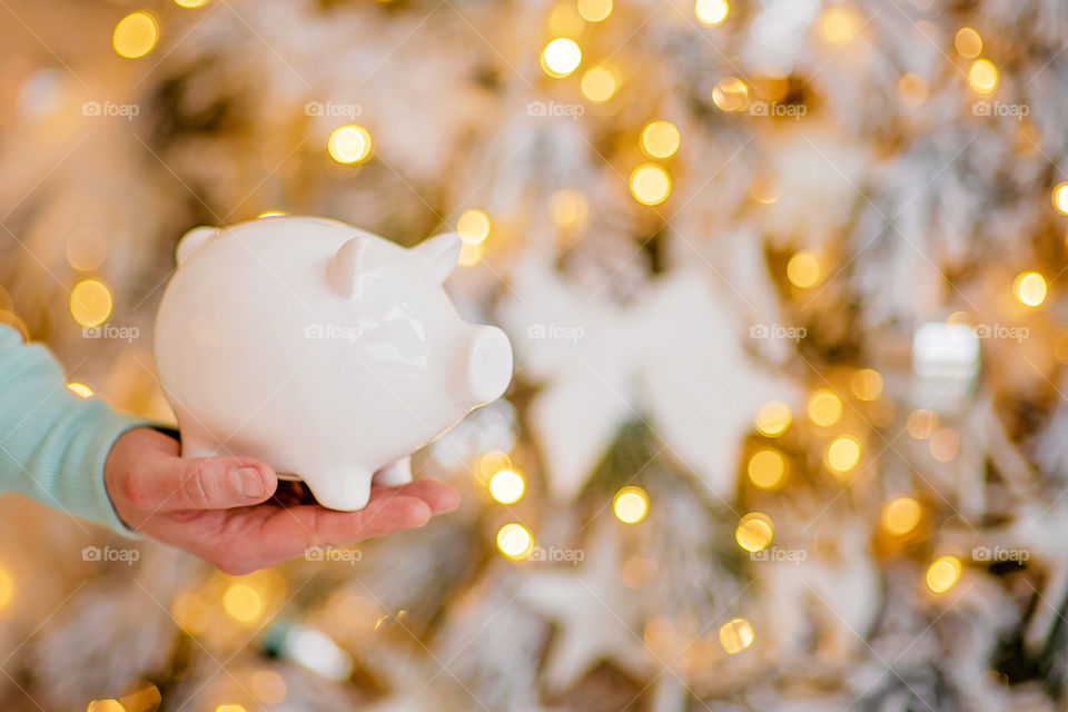 piggy bank with 100 dollars banknote in festive New Year atmosphere of scenery.  Magical bokeh with Christmas tree and bright lights.