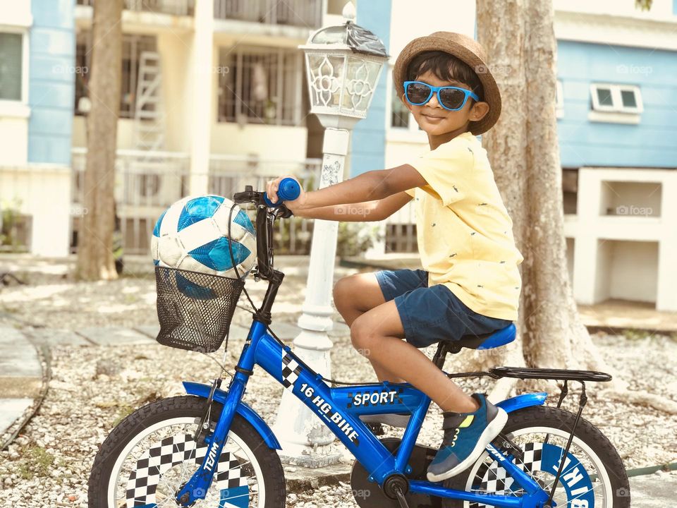 A boy in blue colour bicycle and everything blue with his like football,shoes,eye glasses .