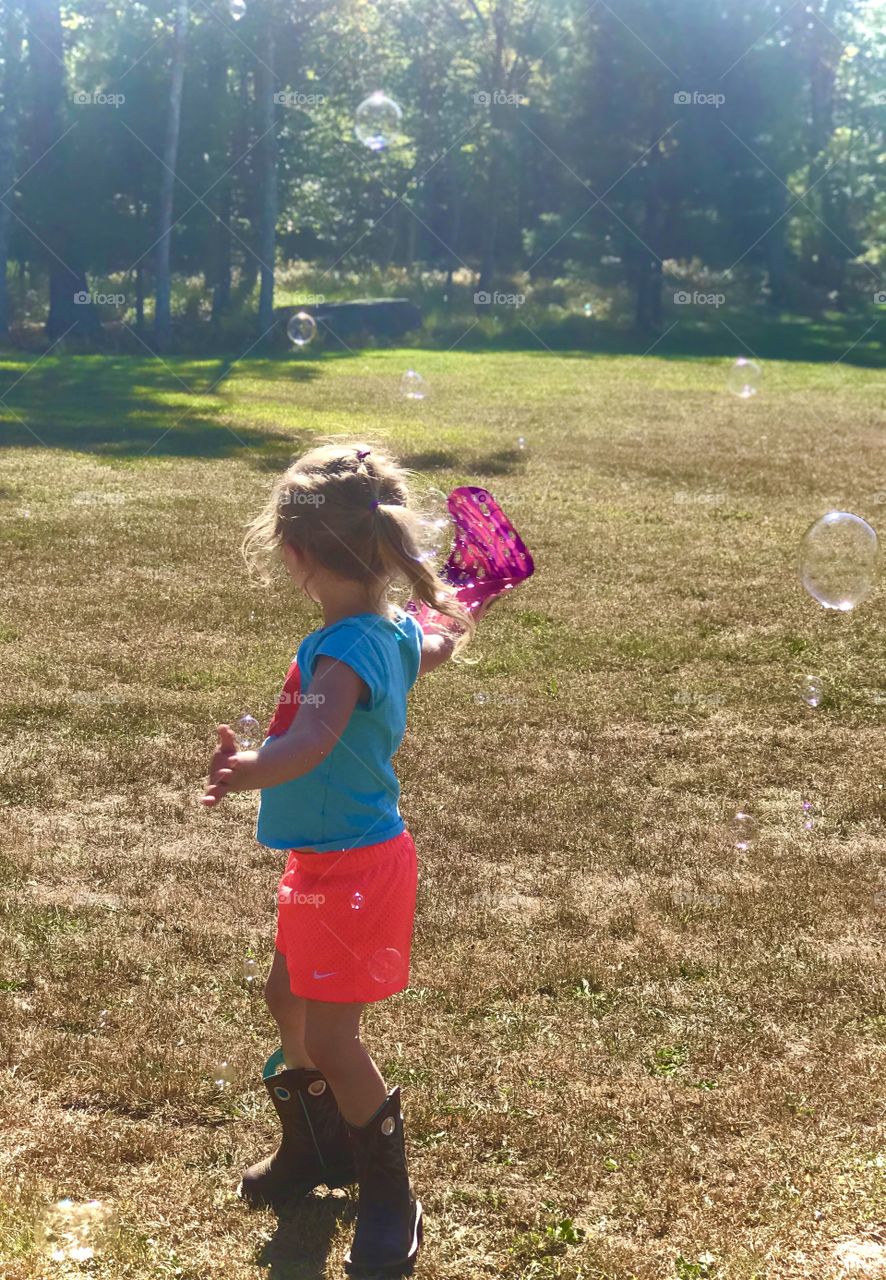 Day photography; 3 year old girl making bubble with a bubble glove in the sunlight and spinning 