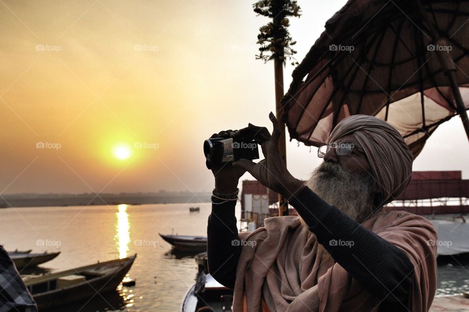 Elderly Indian man using modern tech . Elderly man using tech, Varanasi, River Ganges, India 