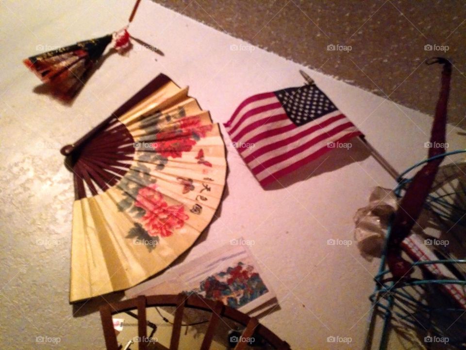 A decorative collage splattering a bedroom wall with colorful fans and bows, a fan wooden framed mirror and the American flag.