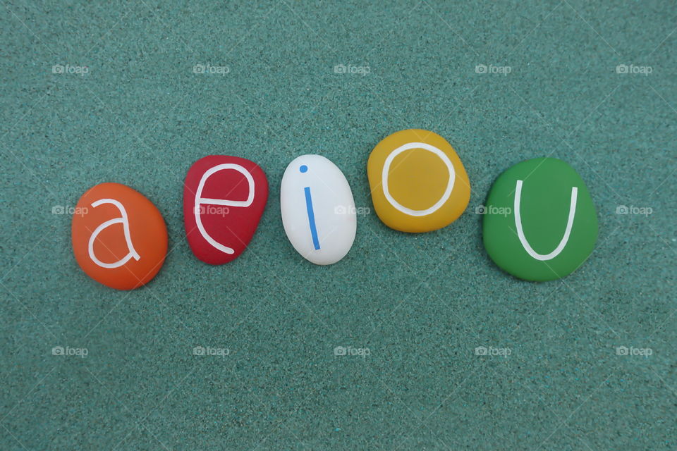 a,e,i,o,u vowel letters composed with colored stones over green sand