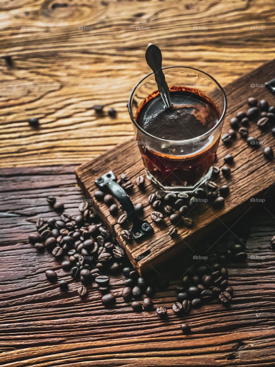 A cup of black hot coffee on a wooden board with scattered coffee beans